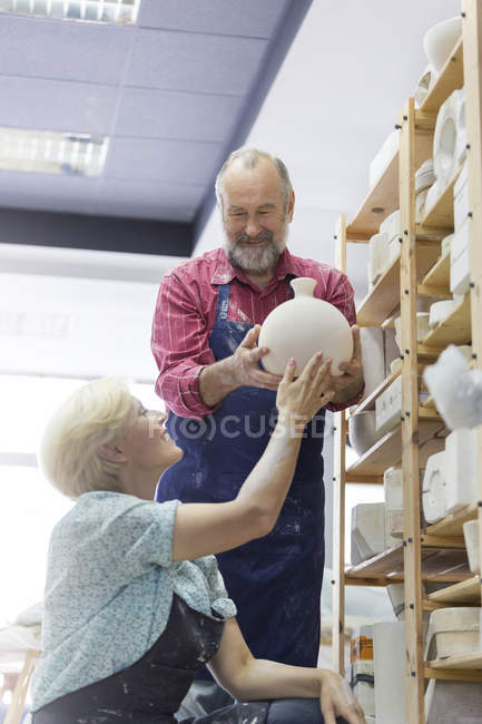 Coppia sorridente che mette vaso di ceramica sullo scaffale in studio — Foto stock