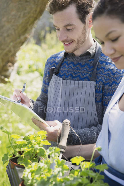 Close up plant nursery workers with clipboard and potted herbs — Stock Photo