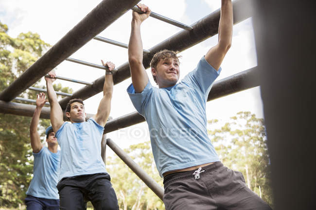 Determined men crossing monkey bars on boot camp obstacle course — Stock Photo