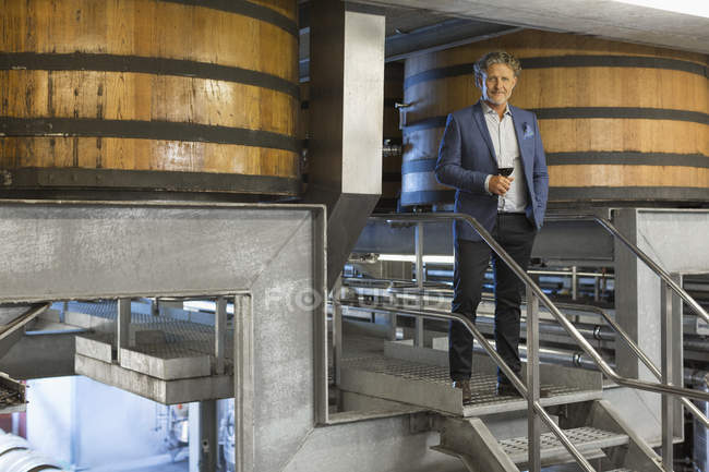 Portrait confident vintner with red wine on platform in winery cellar — Stock Photo