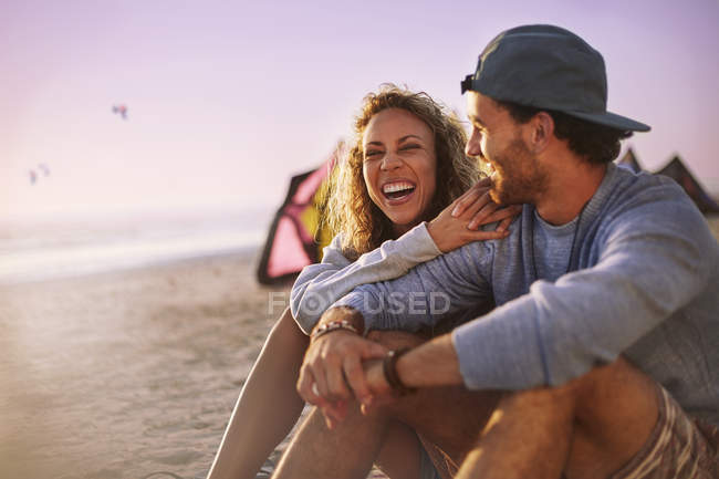 Riendo pareja sentada en la playa - foto de stock