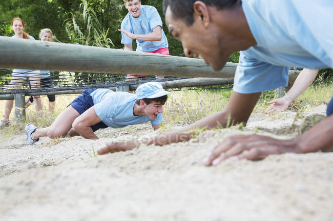 Men crawling under net on boot camp obstacle course — Stock Photo
