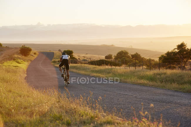 Male triathlete cyclist cycling on sunny rural road at sunrise — Stock Photo