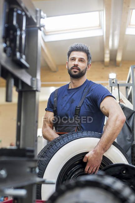 Serious mechanic carrying tire in auto repair shop — Stock Photo