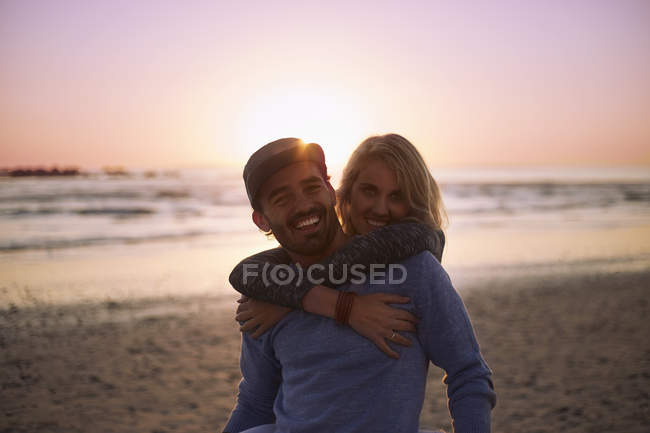 Portrait smiling couple hugging on sunset beach — Stock Photo