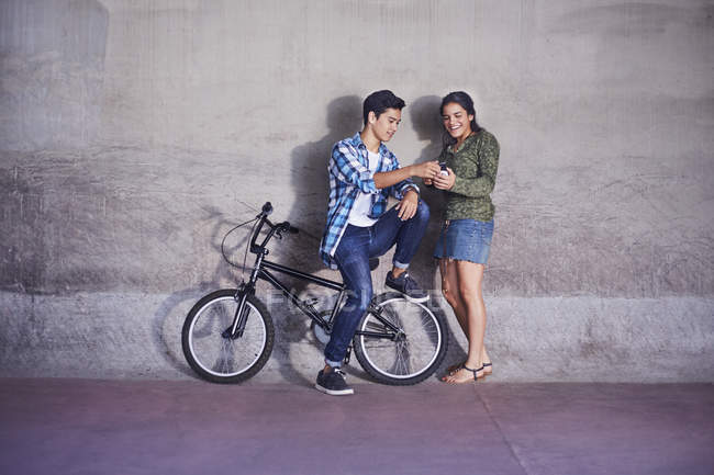 Pareja adolescente con BMX mensajes de texto en bicicleta en la pared - foto de stock