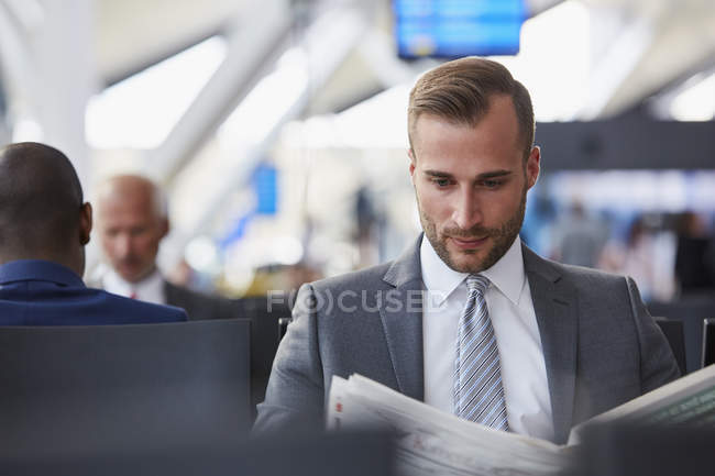 Empresario leyendo periódico en la zona de salida del aeropuerto - foto de stock