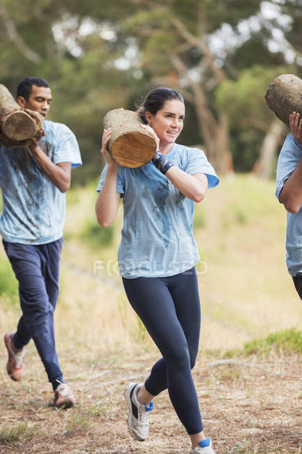 Woman running with log on boot camp obstacle course — Stock Photo