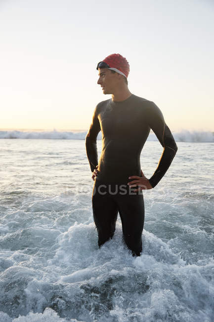 Triathlète masculin en combinaison humide debout dans le surf de l'océan — Photo de stock