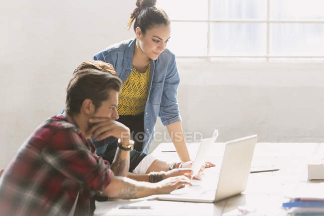 Креативные молодые бизнесмены, работающие за ноутбуком в солнечном офисе — стоковое фото