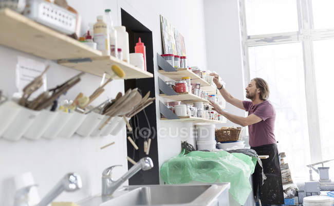Homme naviguant fournitures d'art sur l'étagère en atelier de poterie — Photo de stock