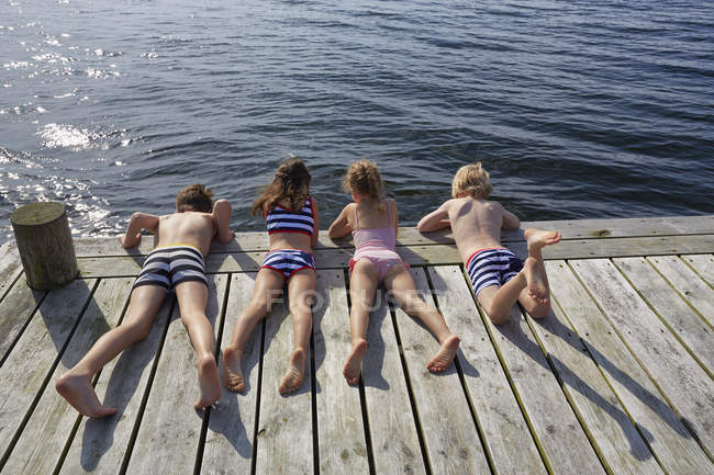 Boys and girls laying on dock looking down at lake — Stock Photo