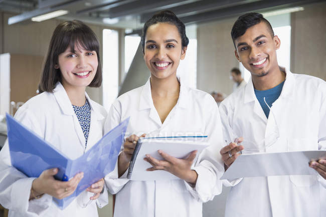Portrait smiling college students in lab coats with notebooks in science laboratory classroom — Stock Photo