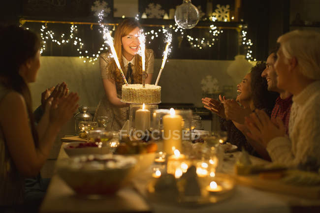 Woman serving Christmas cake with sparkler fireworks to clapping family — Stock Photo