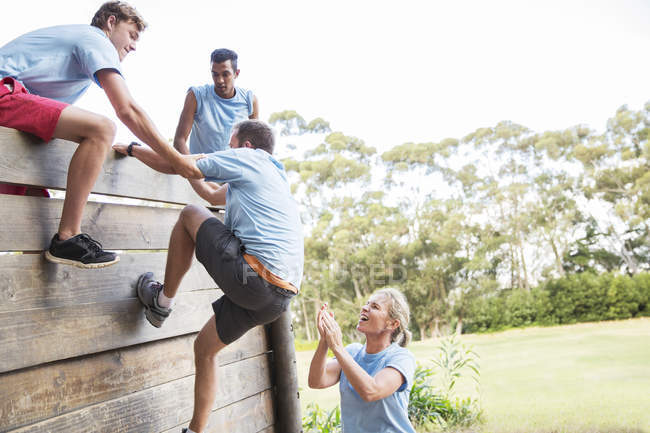 Партнеры по команде помогают человеку перелезть через стену на полосе препятствий учебного лагеря — стоковое фото
