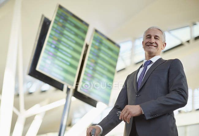 Portrait smiling businessman standing below arrival departure board in airport — Stock Photo