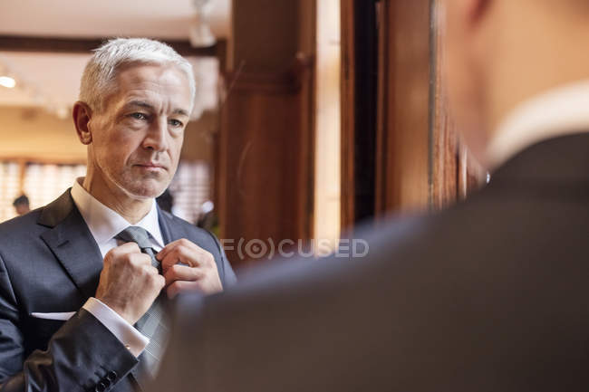 Empresario probándose la corbata en el espejo en la tienda de ropa de hombre - foto de stock