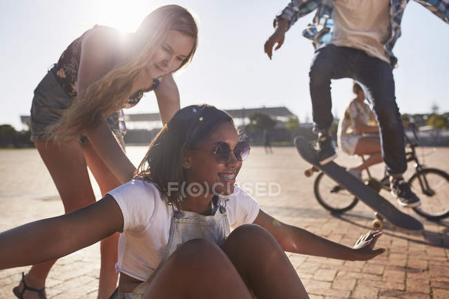 Playful teenage girl pushing friend on skateboard at sunny skate park — Stock Photo