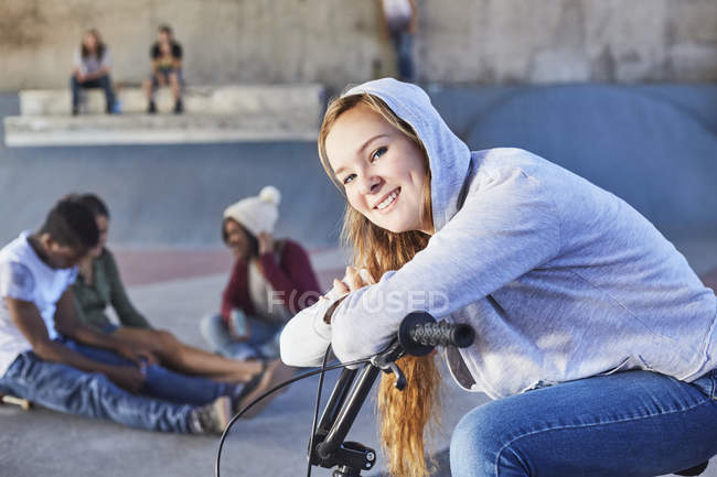 Portrait smiling teenage girl leaning on BMX bicycle at skate park — Stock Photo
