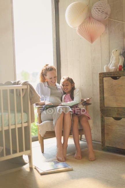 Pregnant mother and daughter reading story book in nursery — Stock Photo