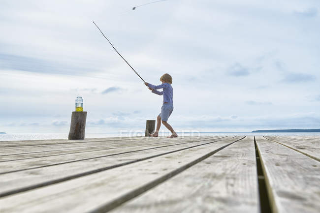 Хлопчик рибалить біля причалу на березі озера — стокове фото