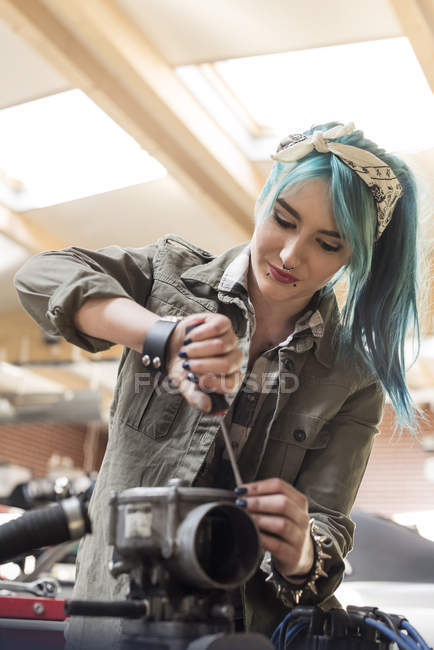 Молодая женщина-механик с синими волосами чинит двигатель автомобиля в автомастерской — стоковое фото