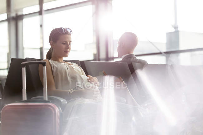 Pregnant woman waiting holding stomach in airport departure area — Stock Photo