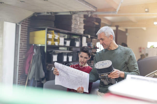 Father and son with plans and engine part rebuilding car in auto repair shop — Stock Photo