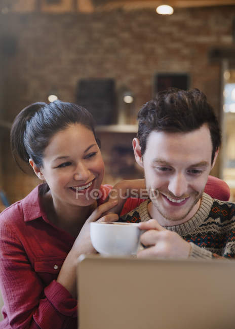 Smiling couple drinking cappuccino at laptop in cafe — Stock Photo