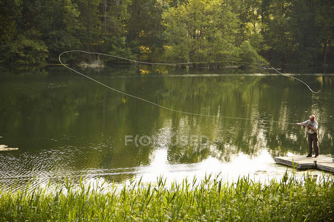 Старший чоловік літає риболовлею на зеленому літньому озері — стокове фото