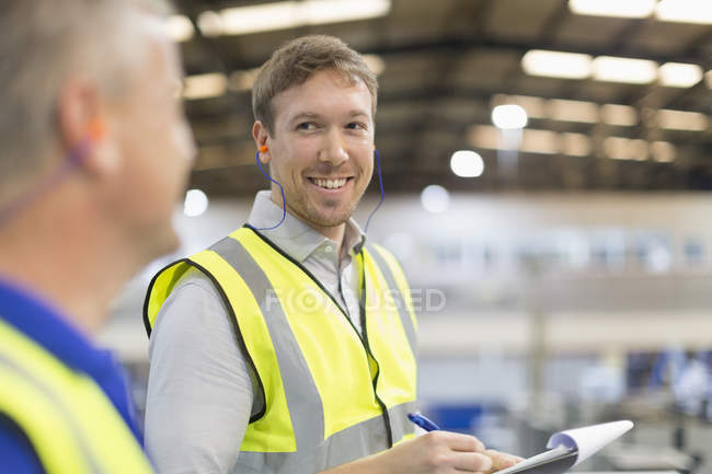 Supervisor with clipboard smiling at worker in steel factory — Stock Photo