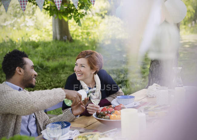 Pareja sonriente vertiendo vino en la mesa de fiesta del jardín - foto de stock