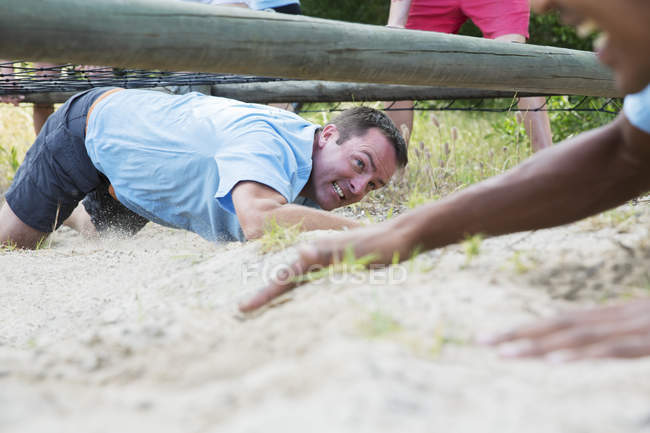 Determinado hombre arrastrándose bajo la red en campo de entrenamiento carrera de obstáculos - foto de stock