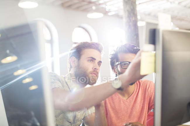 Hommes d'affaires occasionnels concentrés travaillant à l'ordinateur dans un bureau ensoleillé — Photo de stock