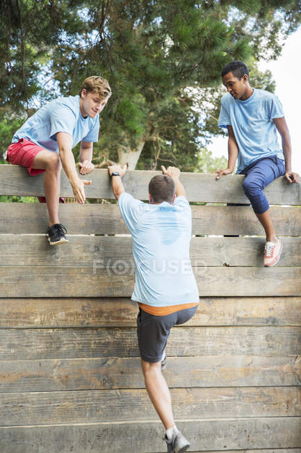 Colegas de equipe ajudando o homem sobre a parede no campo de inicialização curso de obstáculo — Fotografia de Stock