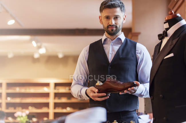 Portrait confident businessman holding dress shoe in menswear shop — Stock Photo