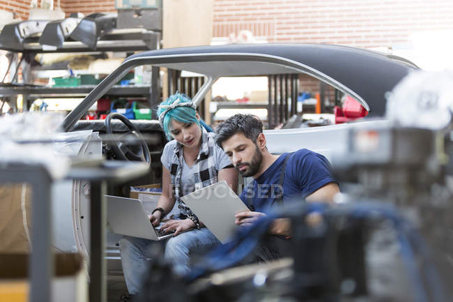 Mécanique travaillant avec presse-papiers et ordinateur portable dans l'atelier de réparation automobile — Photo de stock