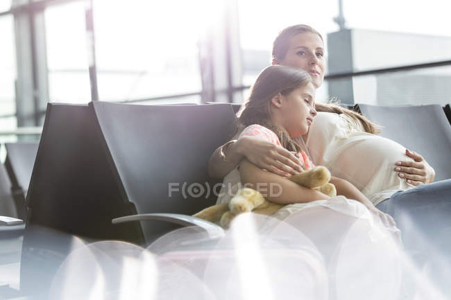 Schwangere Mutter und schlafende Tochter warten im Abflugbereich des Flughafens — Stockfoto