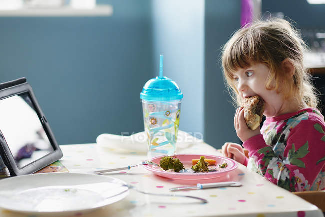 Menina comendo hambúrguer e assistindo tablet digital — Fotografia de Stock