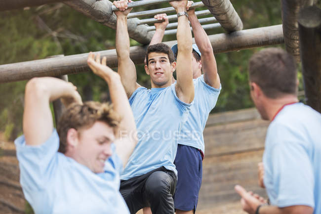 Homme déterminé balançant sur des barres de singe sur le parcours d'obstacle du camp d'entraînement — Photo de stock