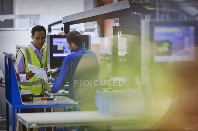 Vorgesetzter und Arbeiter diskutieren Papierkram an Maschine in Stahlwerk — Stockfoto