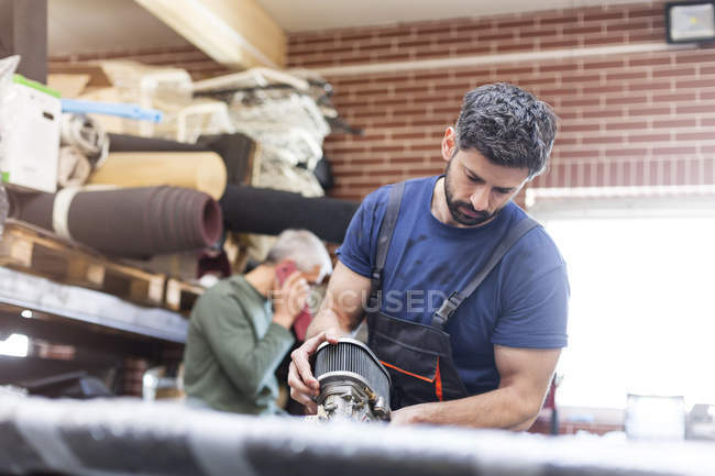 Mécanicien concentré avec la pièce de moteur de voiture dans l'atelier de réparation automobile — Photo de stock