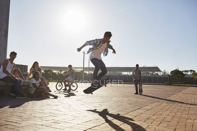 Друзі дивляться хлопчика-підлітка, який перевертає скейтборд на сонячному скейт-парку — стокове фото