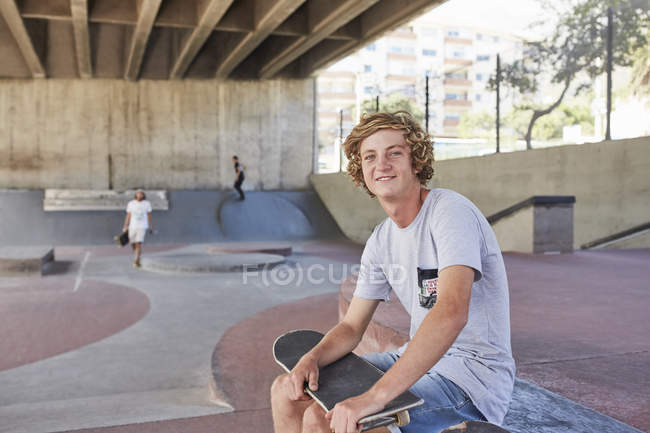 Retrato sorridente adolescente com skate no parque de skate — Fotografia de Stock