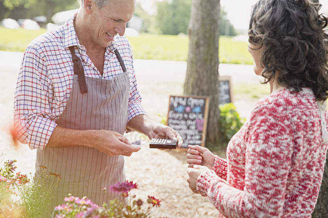 Woman watching plant nursery worker using credit card reader — Stock Photo