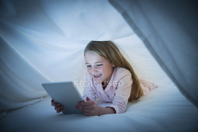 Lächelndes Mädchen mit digitalem Tablet unter Laken — Stockfoto