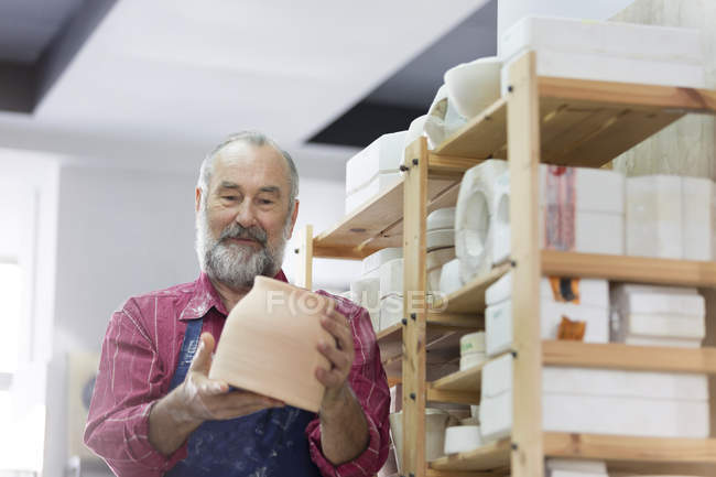 Hombre mayor examinando tazón de cerámica en el estudio - foto de stock