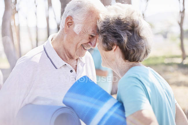 Affectionate senior couple holding yoga mats in park — Stock Photo