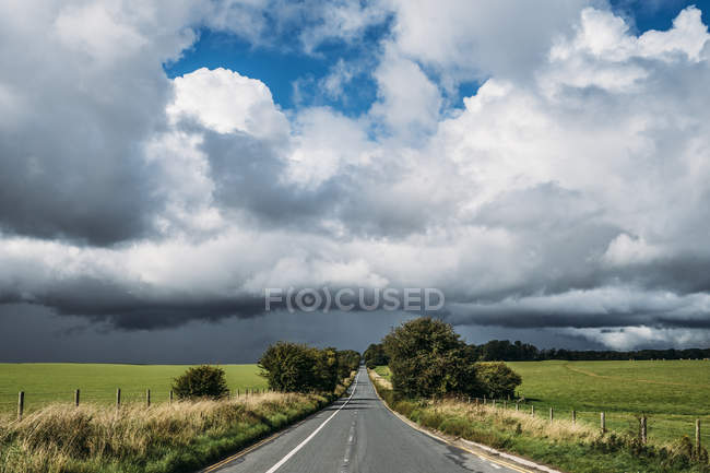 Fluffy clouds over countryside and rural road — Stock Photo
