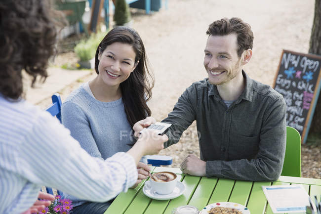 Garçonete entregando leitor de cartão de crédito para casal no café ao ar livre — Fotografia de Stock